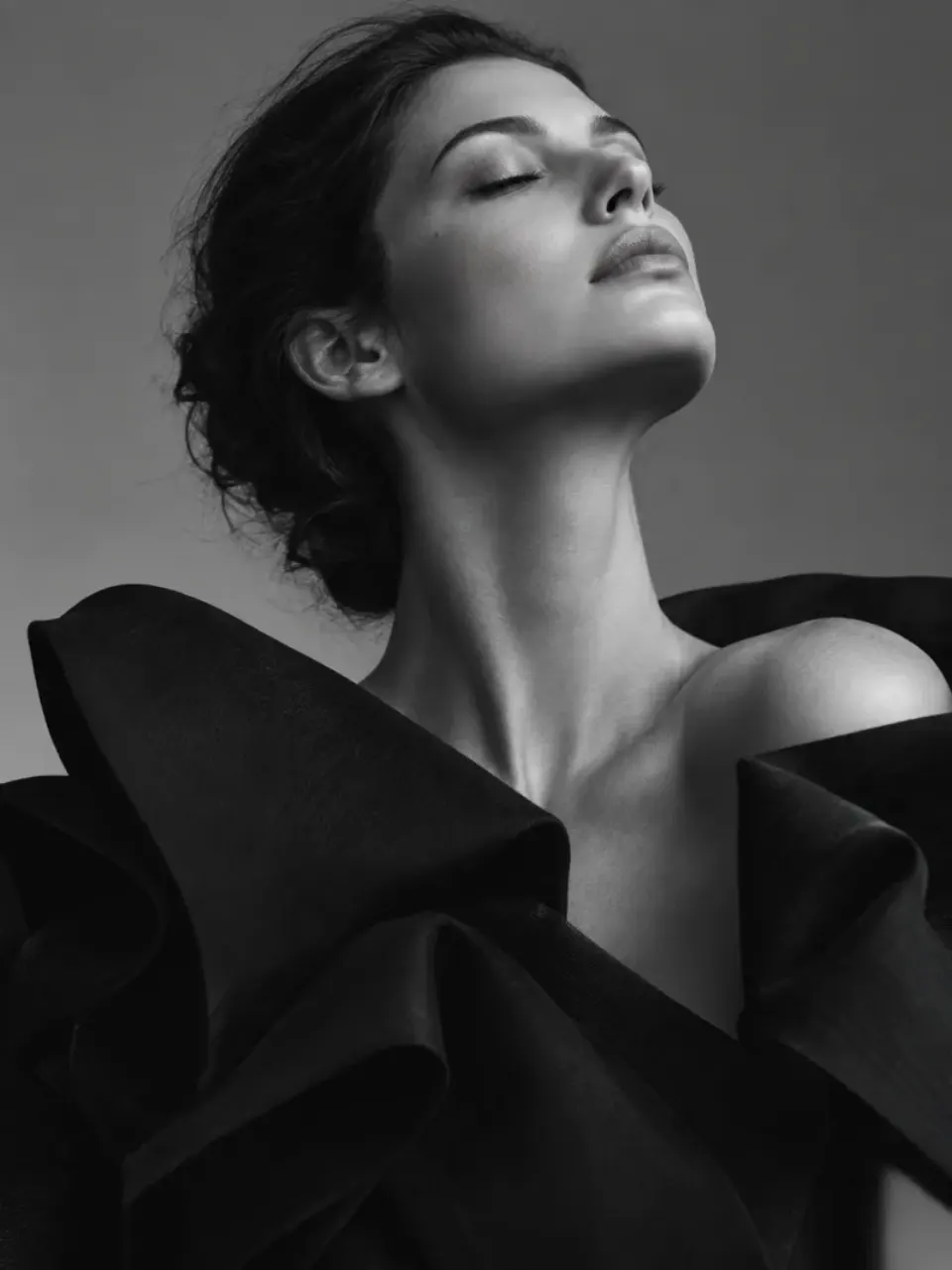 Black and white portrait of an adult model wearing a sculptural black garment